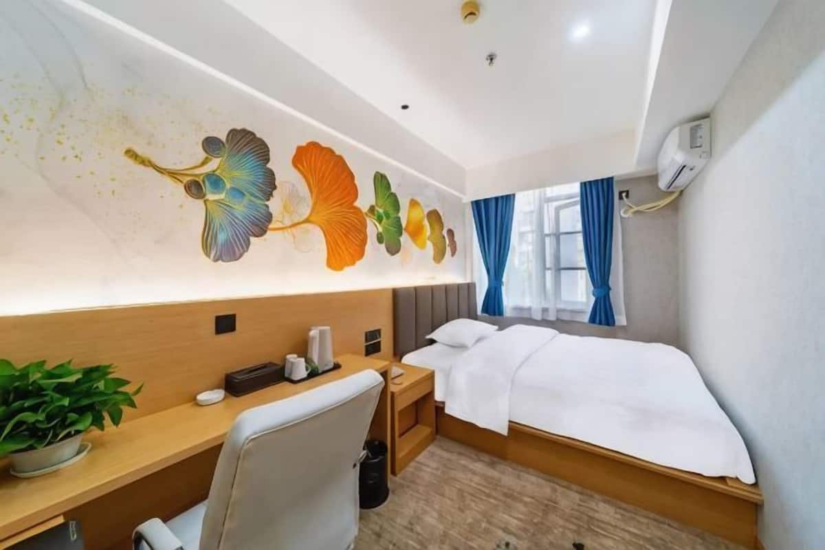 A hotel room with a bed, desk, chair, and a wall with a floral mural.