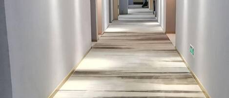 Un pasillo largo y estrecho con alfombra estampada y paredes de colores claros.