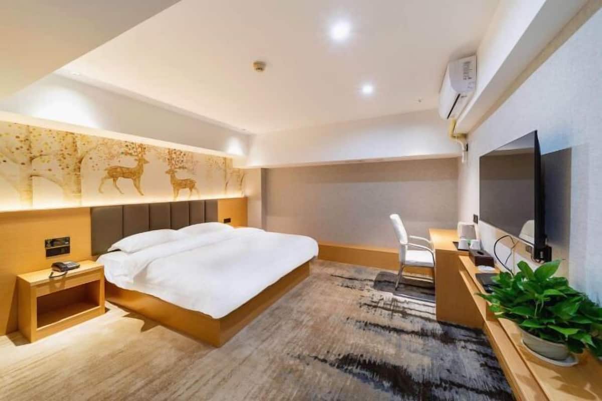 A modern hotel room with a large bed, bedside table, TV, and a desk with a chair.