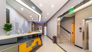 Un espace d’accueil d’hôtel au design moderne, comprenant un comptoir d’accueil, un escalier et un ascenseur.