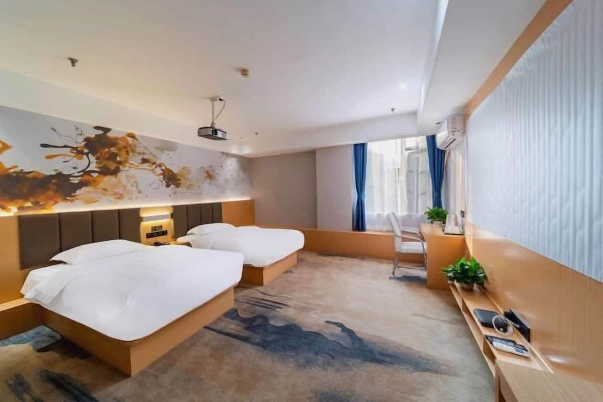 A modern hotel room with a large bed, bedside tables, a desk, and a large window.