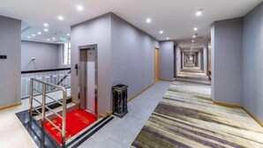 Un couloir d’hôtel avec un tapis rouge, une main courante en métal et un tapis à motifs.