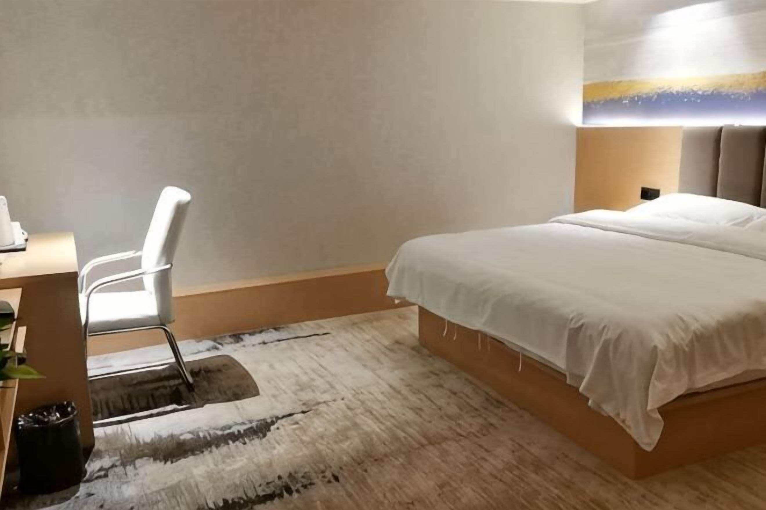 A hotel room with a bed, a desk with a chair, and a rug.