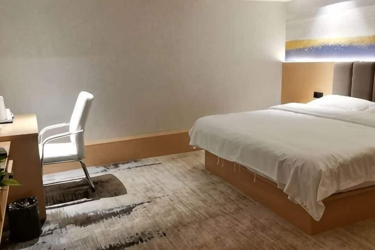 A hotel room with a bed, a desk with a chair, and a rug.