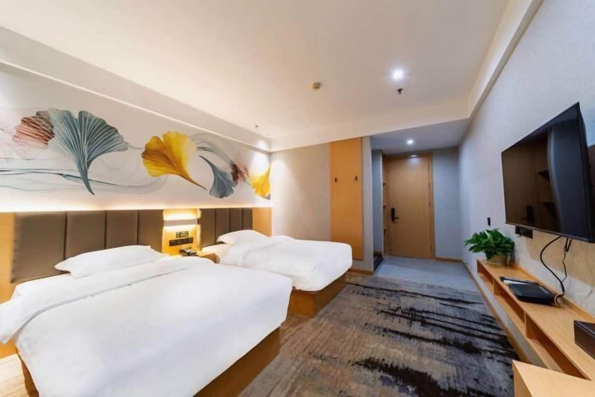 A hotel room with two beds, a large wall-mounted TV, and a ceiling with recessed lighting.