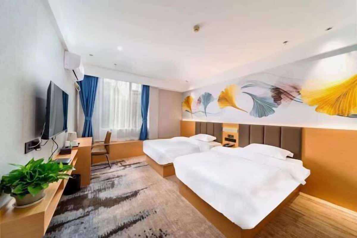 A hotel room with two beds, a desk with a chair, a TV, and a large floral mural on the wall.