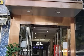 A hotel entrance with a glass door, a sign above the door, and a potted plant to the left. - Jin'gutian Hotel (Wuhan)