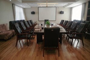A conference room with a long table, multiple chairs, a projector screen, and a potted plant. - Haoyun Hotel (Menyuan)