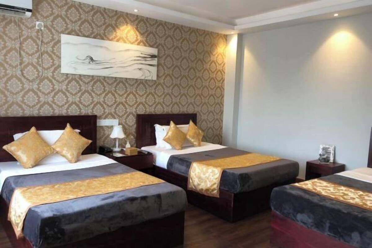 A hotel room with two beds, a large painting on the wall, and a patterned wallpaper.