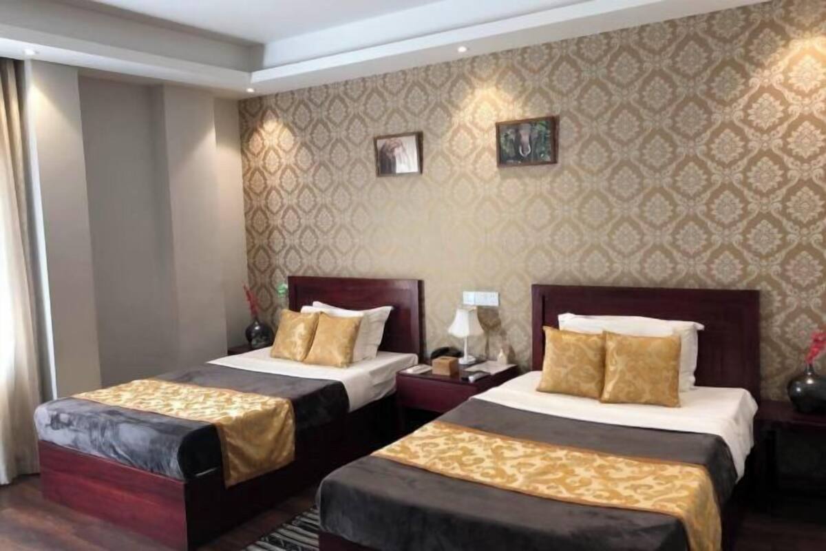 A hotel room with two beds, a patterned wallpaper, and a nightstand with a lamp.