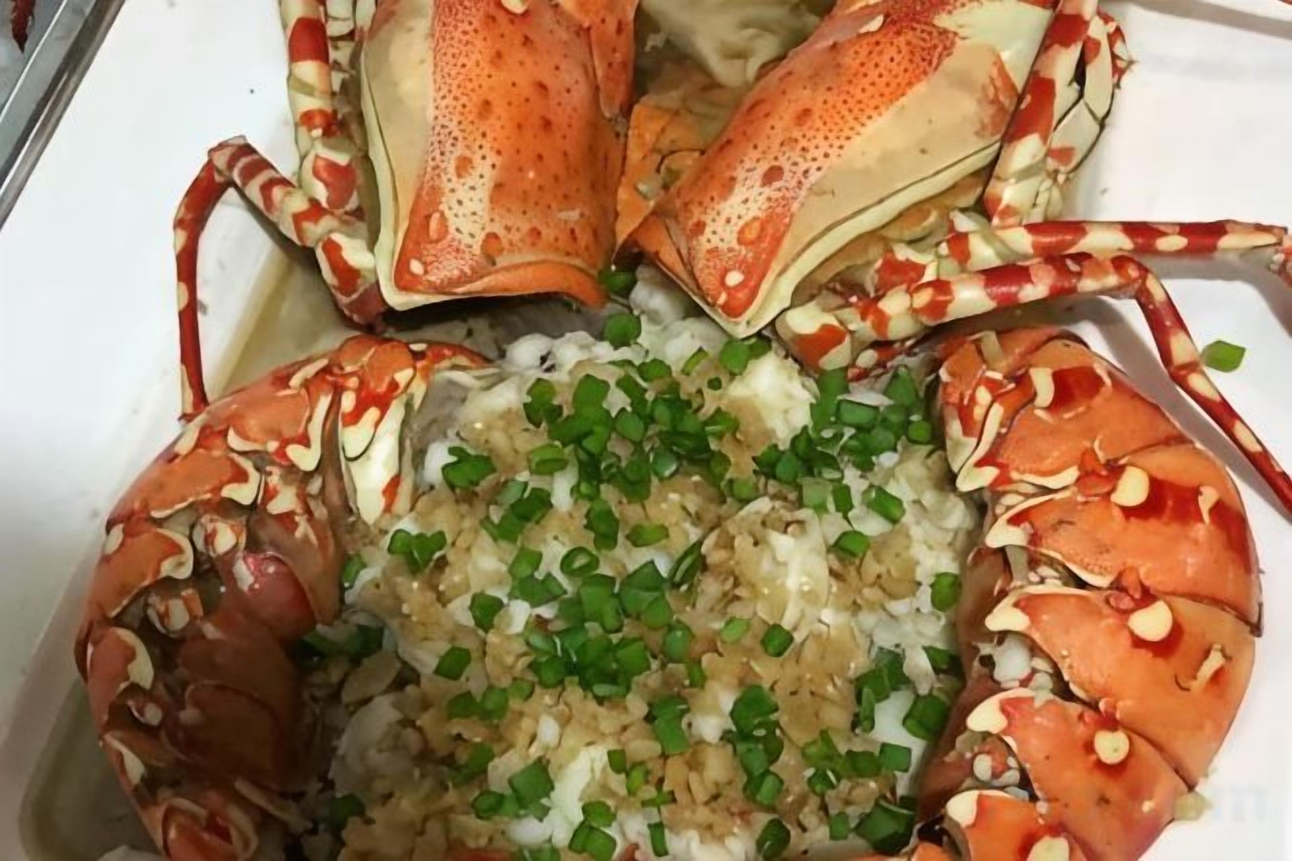 A lobster with its claws intact, garnished with chopped green onions, served on a white plate.