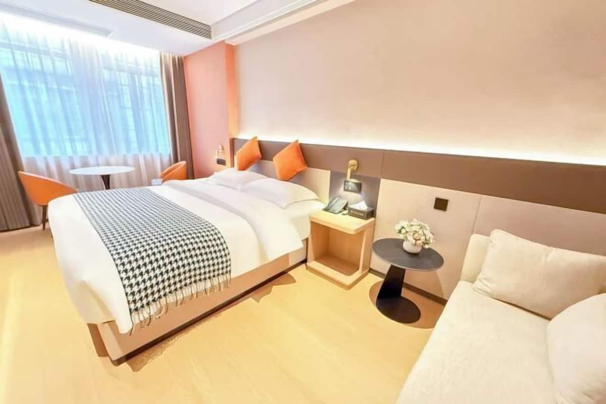 Une chambre d’hôtel moderne avec un grand lit, des tables de chevet, une petite table ronde ornée d’un vase et un canapé.