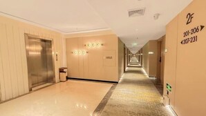 A hotel hallway with an elevator, a patterned carpet, and directional signs on the walls.