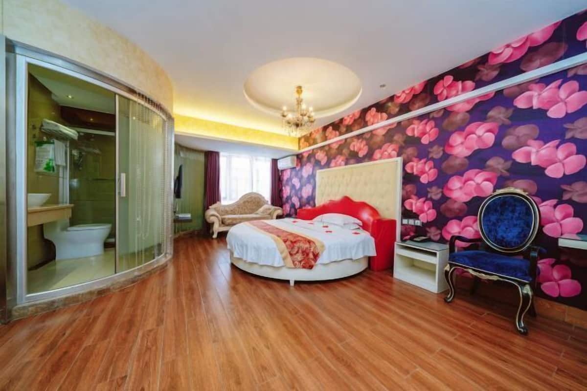 Une chambre à coucher avec un lit rond, un fauteuil rouge, un lustre et un papier peint à motifs floraux.