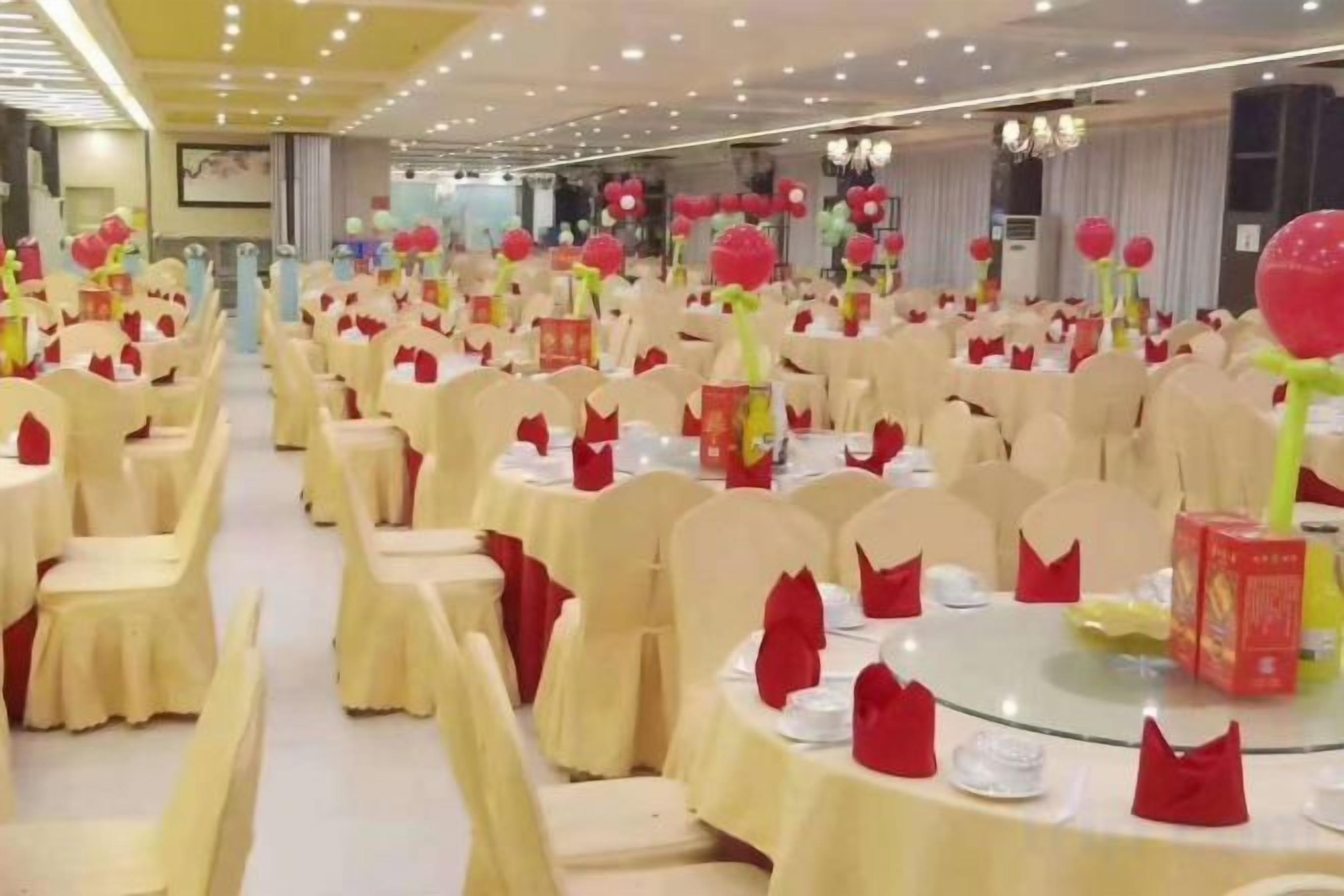 A banquet hall with round tables, chairs, and red decorations.