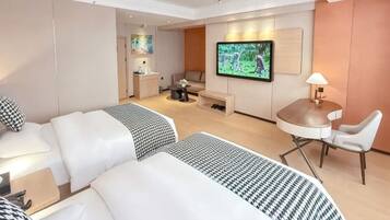 A hotel room with two beds, a TV, a desk, a chair, and a small kitchenette.