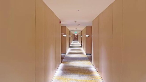A long, narrow hotel corridor with a patterned carpet and beige walls.