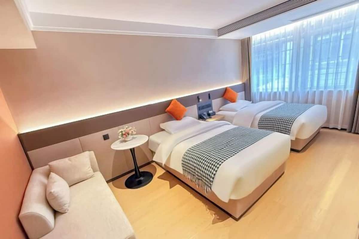 Une chambre d’hôtel moderne avec un grand lit, un canapé, une petite table et une grande fenêtre avec des rideaux.