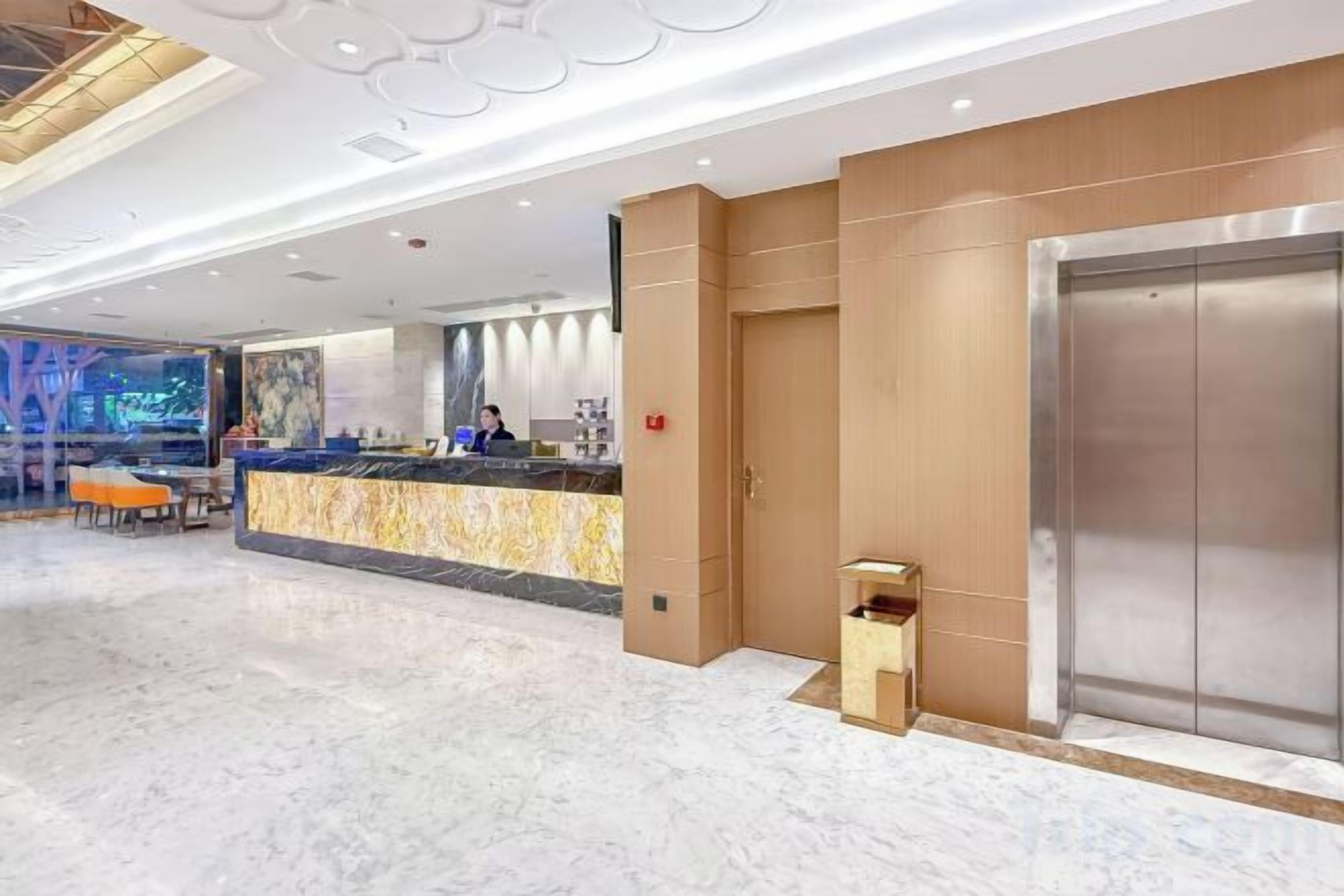 A hotel lobby with a reception desk, a marble floor, and an elevator.