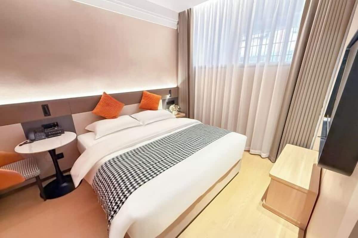 Une chambre d’hôtel avec un lit, une petite table, une chaise, un téléviseur et une fenêtre avec des rideaux.