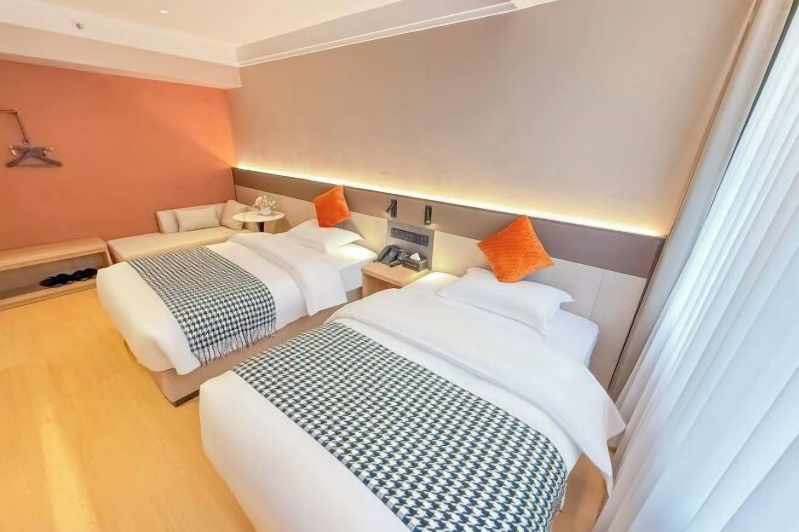 A hotel room with two beds, a bedside table with a lamp, a small table, and a wall-mounted TV.