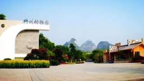 A spacious courtyard with a modern building featuring a sign, surrounded by lush greenery and mountains in the background.