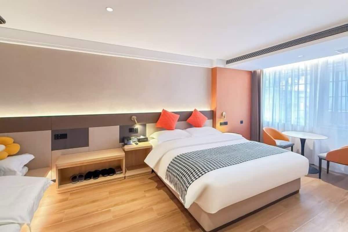 Une chambre d’hôtel avec un grand lit, des tables de chevet, un petit bureau, une chaise et une fenêtre avec des rideaux.
