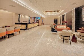 A hotel lobby with a reception desk, seating area, and a modern chandelier.