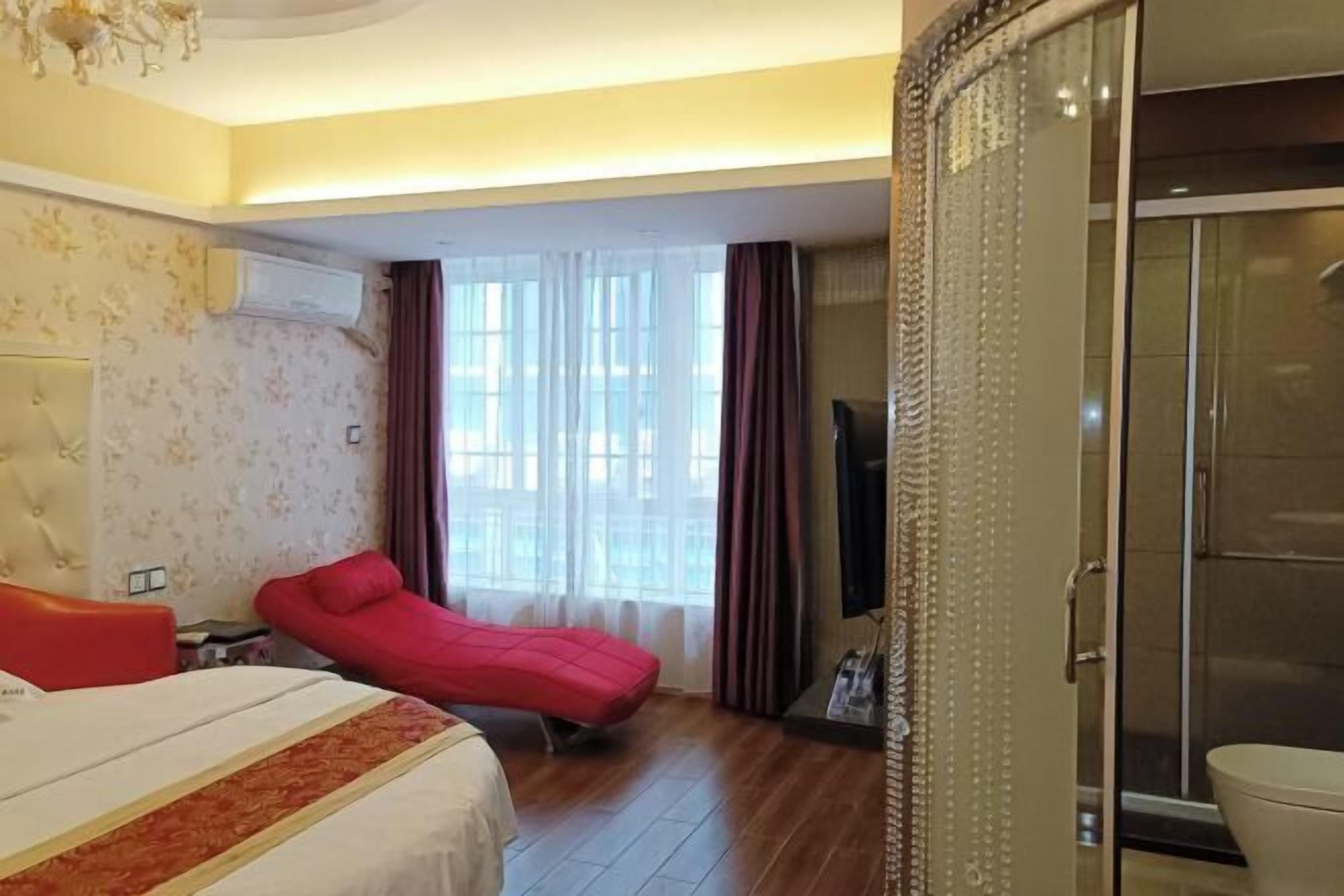 Une chambre d’hôtel avec un lit, un canapé rouge, une télévision et une porte-fenêtre coulissante donnant sur un espace douche.