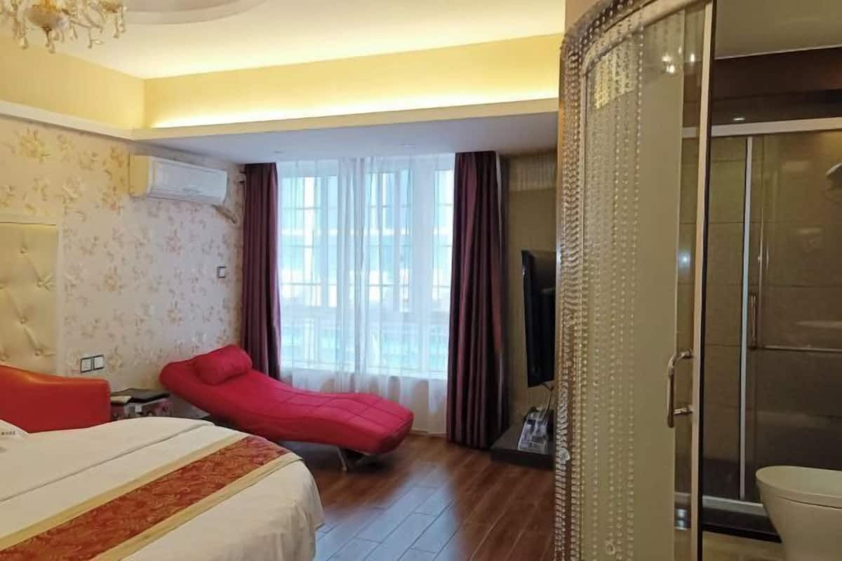 Une chambre d’hôtel avec un lit, un canapé rouge, une télévision et une porte-fenêtre coulissante donnant sur un espace douche.