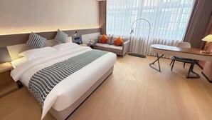 A hotel room with a large bed, a sofa, a dining table, and a window with curtains.