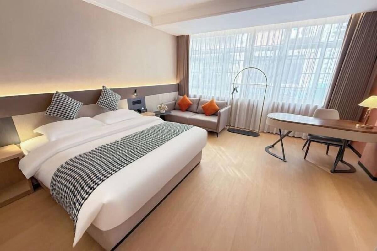 Une chambre d’hôtel avec un grand lit, un canapé, une table à manger et une fenêtre avec des rideaux.