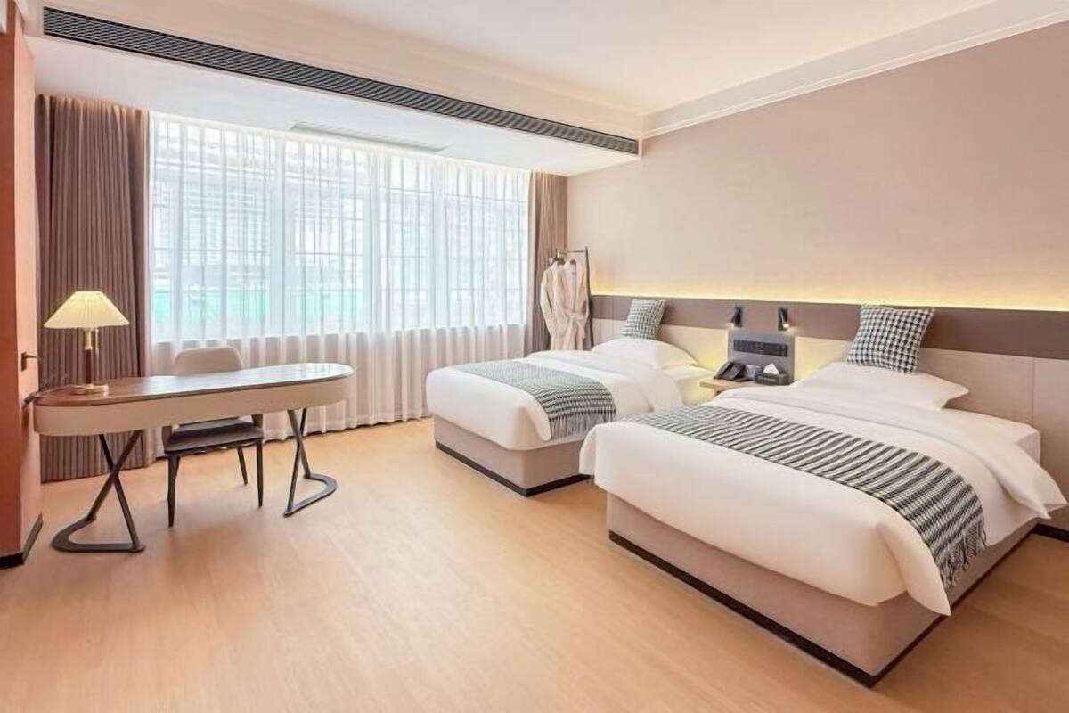 Une chambre d’hôtel avec deux lits, un bureau et une fenêtre avec des rideaux.