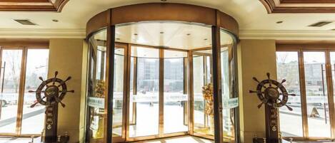 A lobby with a glass revolving door, two ship's wheel decorations, and a polished floor.