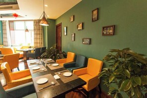 Un espace repas avec une longue table, plusieurs chaises et un mur vert orné de tableaux encadrés.