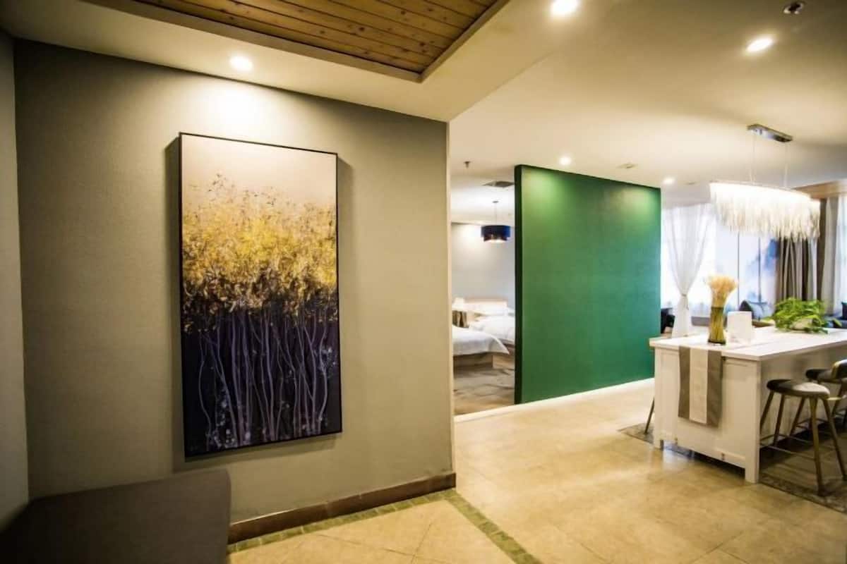 Una habitación de hotel moderna con un cuadro abstracto grande en la pared, un separador verde y una zona de comedor con una mesa blanca y taburetes de bar.