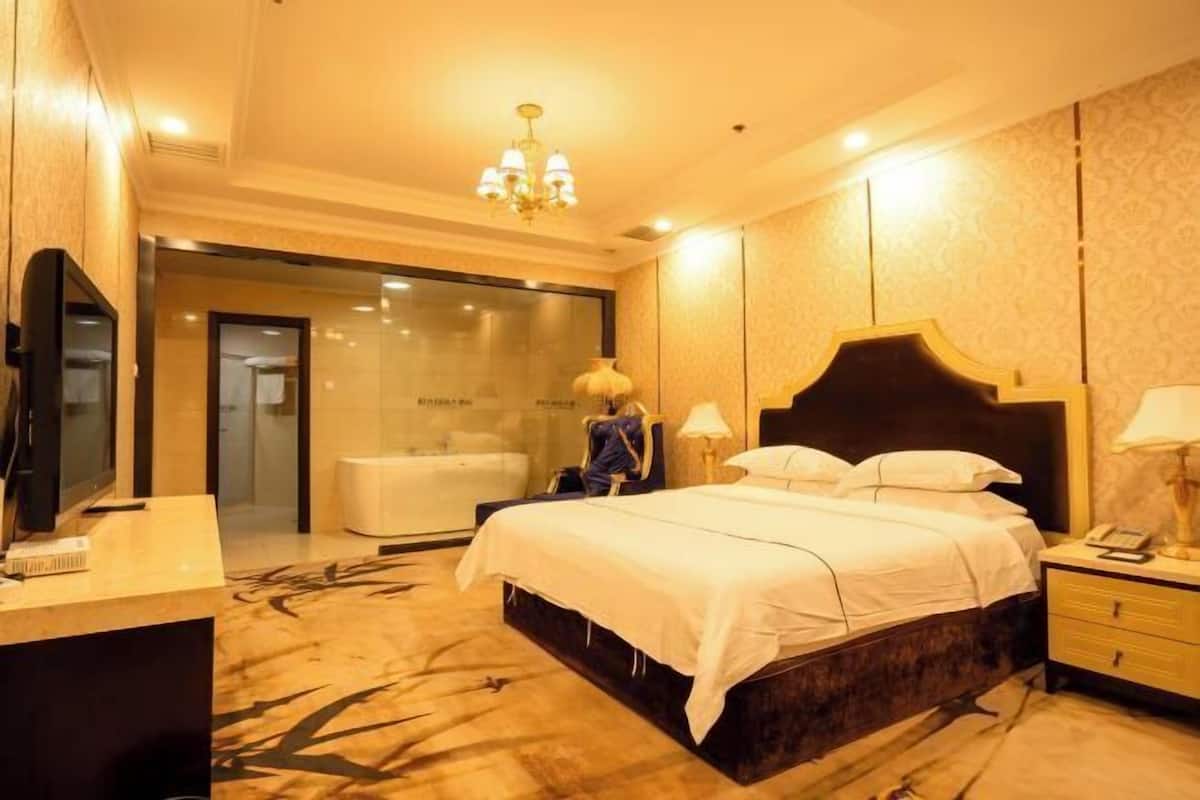 Habitación de hotel con una cama grande, un escritorio, una silla, un televisor, un baño y un candelabro.
