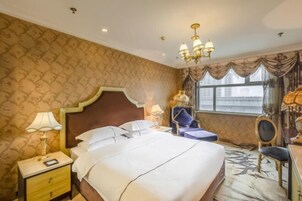 Habitación de hotel con una cama grande, una mesita de noche, una lámpara, una silla y una ventana con cortinas.