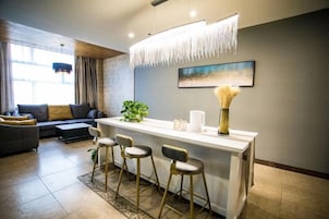 Una sala de estar moderna con un sofá, una mesa de centro, un rincón comedor con taburetes y un cuadro en la pared.