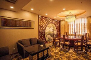 A hotel room with a dining table, chairs, a sofa, and a decorative wall.
