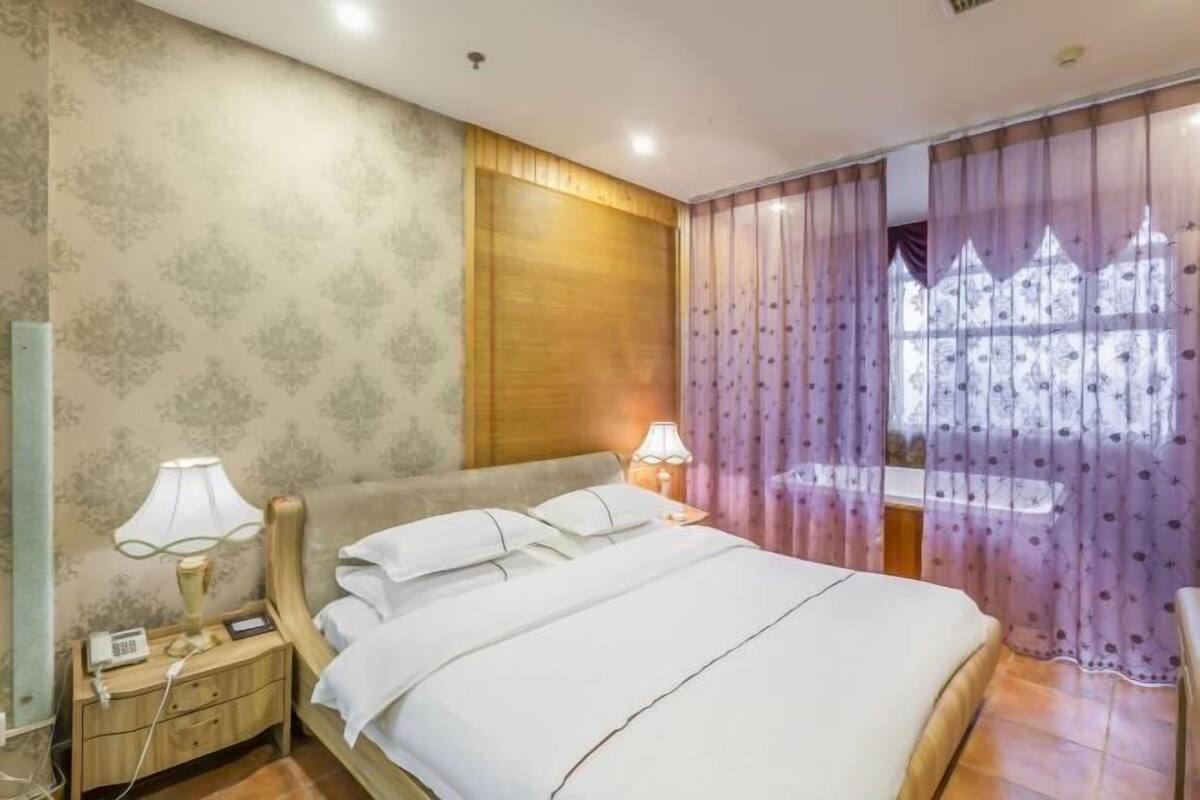 Habitación de hotel impecable con cama, lámparas de noche, mesita de noche y ventana con cortinas.