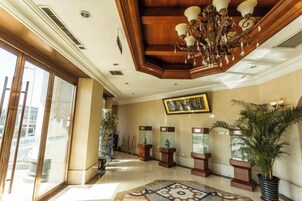 Un vestíbulo de hotel con una araña, un cuadro grande enmarco y plantas en macetas.