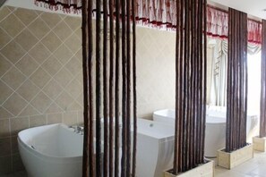 Een badkamer met een groot bad, een kleinere wastafel en een spiegel.