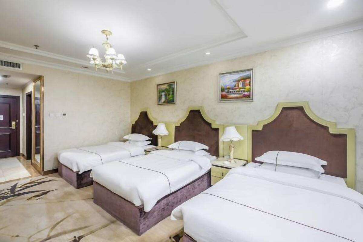 Habitación de hotel con tres camas, una araña y obras de arte en las paredes.