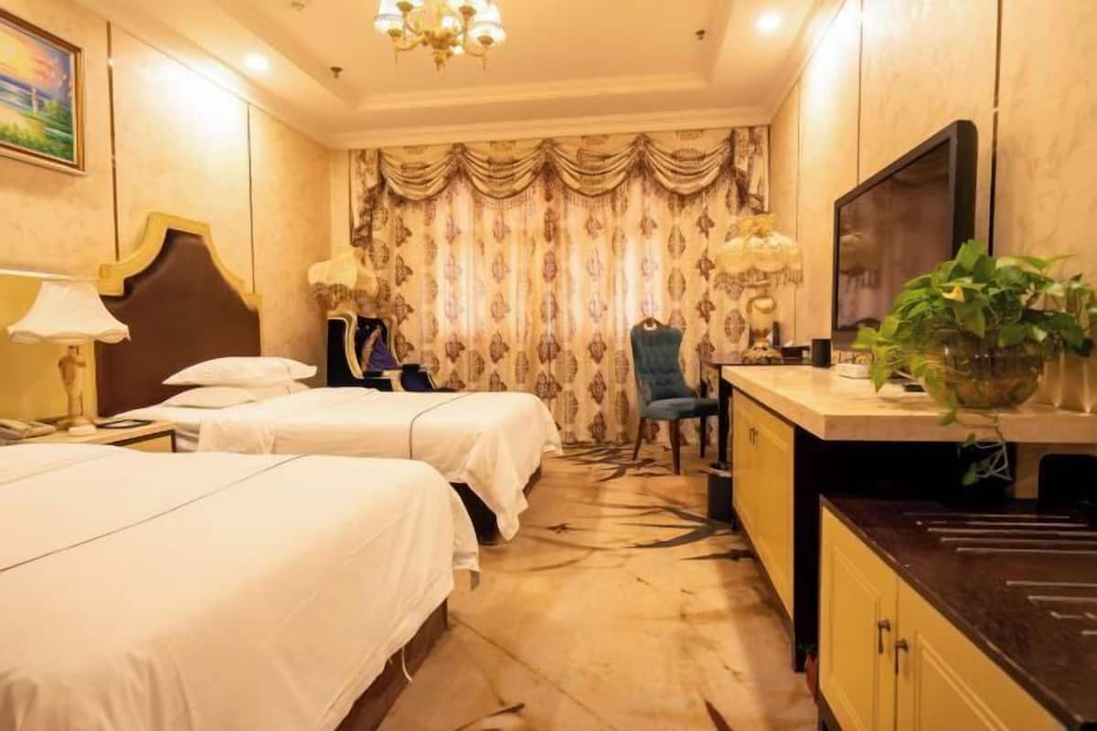 Habitación de hotel con dos camas, un escritorio, una silla, un televisor y un ventanal con cortinas.