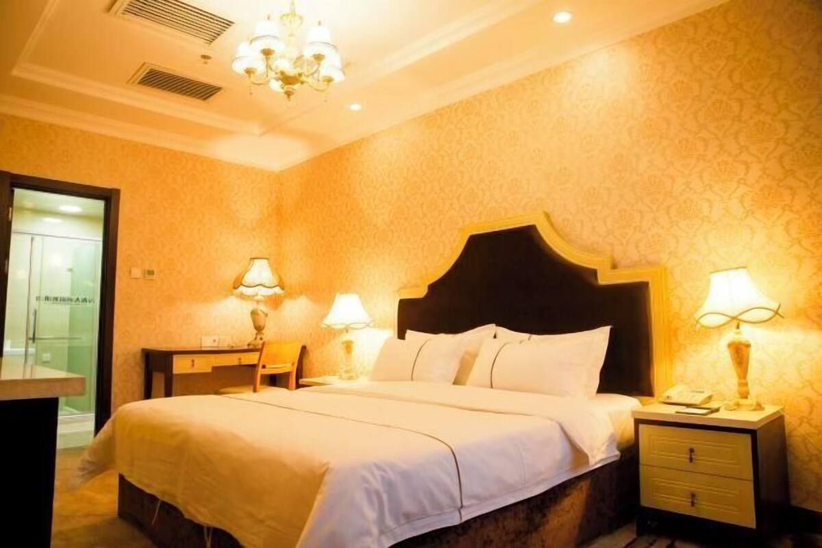 Una habitación de hotel con una cama grande, dos mesitas de noche con lámparas, un cabecero de madera y un escritorio pequeño con una silla.