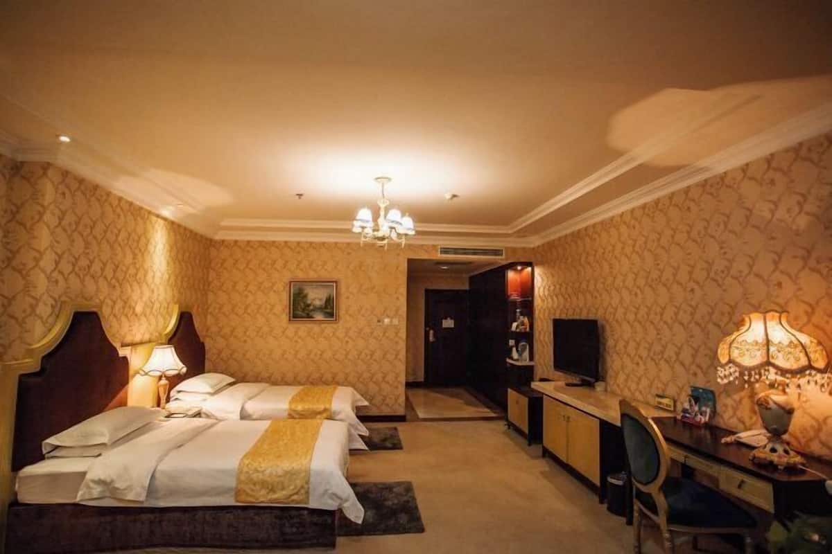 Habitación de hotel con dos camas, un escritorio, una silla, un televisor y un candelabro.
