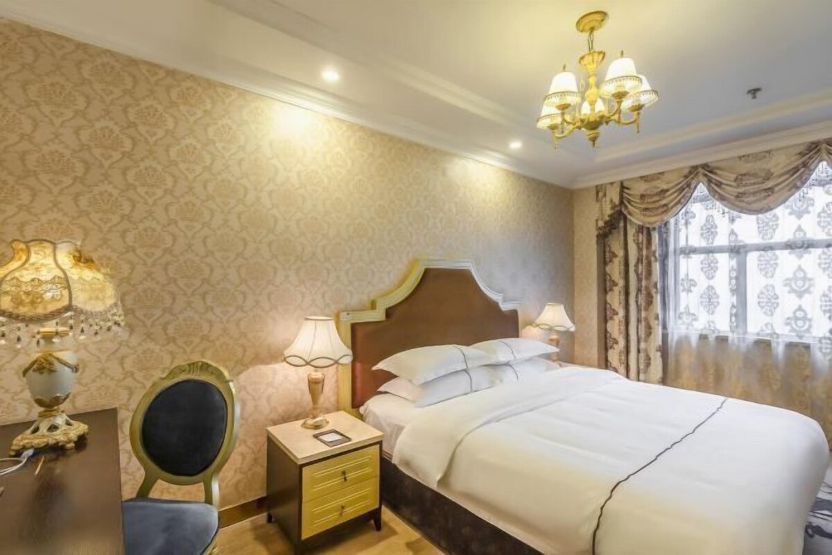 A hotel room with a large bed, a nightstand with a lamp, a chair, and a mirror.