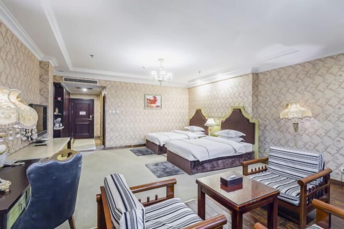 A hotel room with a double bed, two bedside tables, a desk with a chair, and a patterned wall.