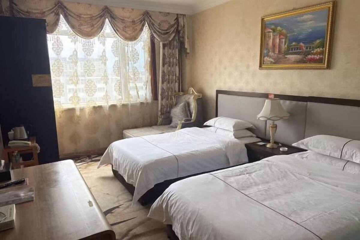 Una habitación de hotel con dos camas, un escritorio, una silla, una lámpara y un cuadro en la pared.